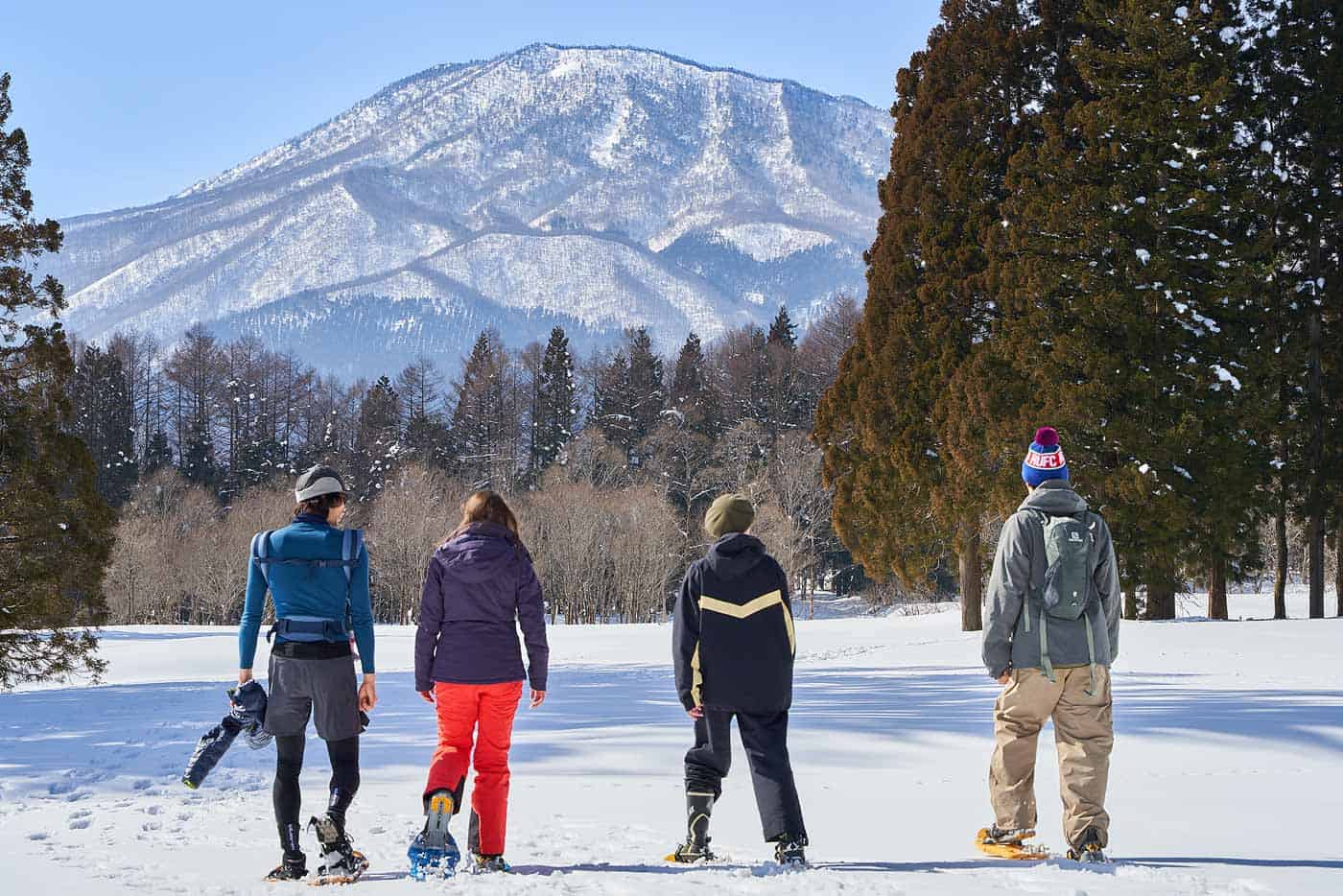 group of people snowshoeing through a open field in front of a mountain